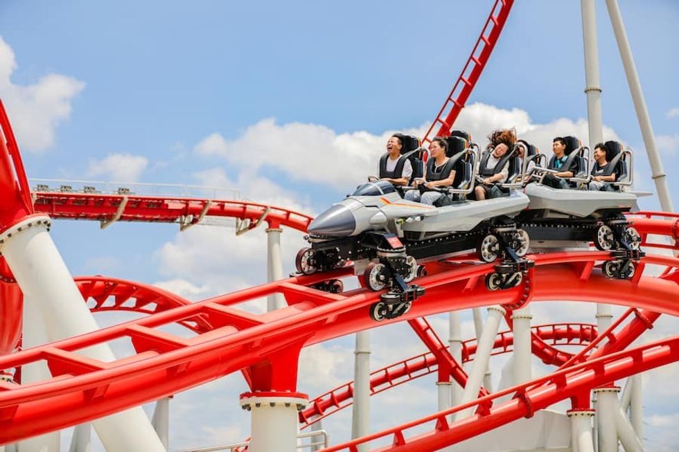 8 young people in jet-shaped roller coaster cars screaming rolling down a red track