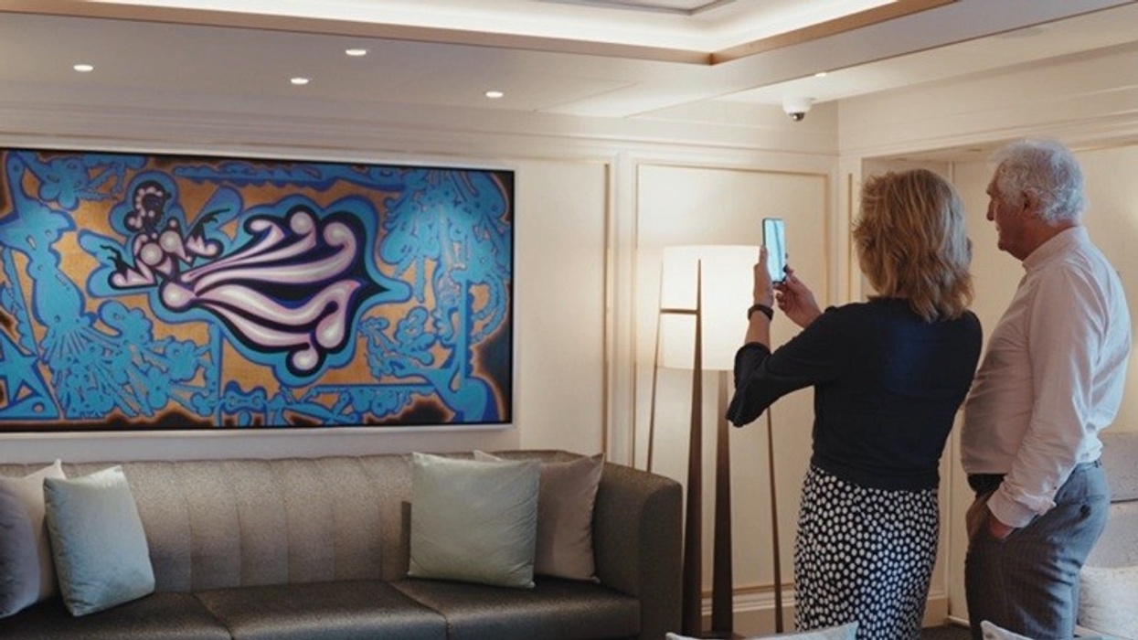 A couple admires and photographs a vibrant abstract painting in a modern living room.