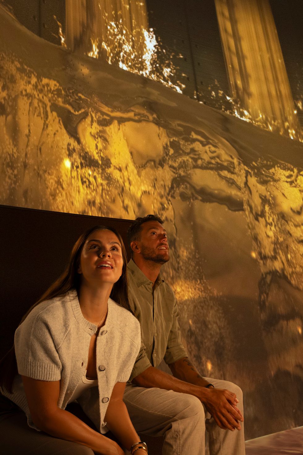 A couple gazes at a stunning golden light display on a large screen.