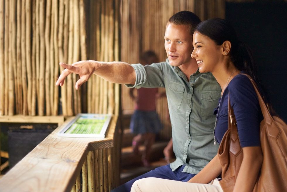 A couple smiling, looking at a zoo exhibit, while the man points at something.