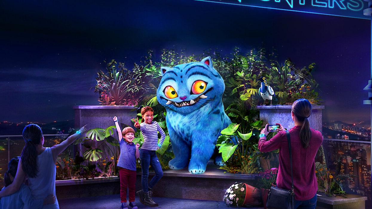 A family poses with a giant cartoonish blue cat in a nighttime, plant-filled setting.