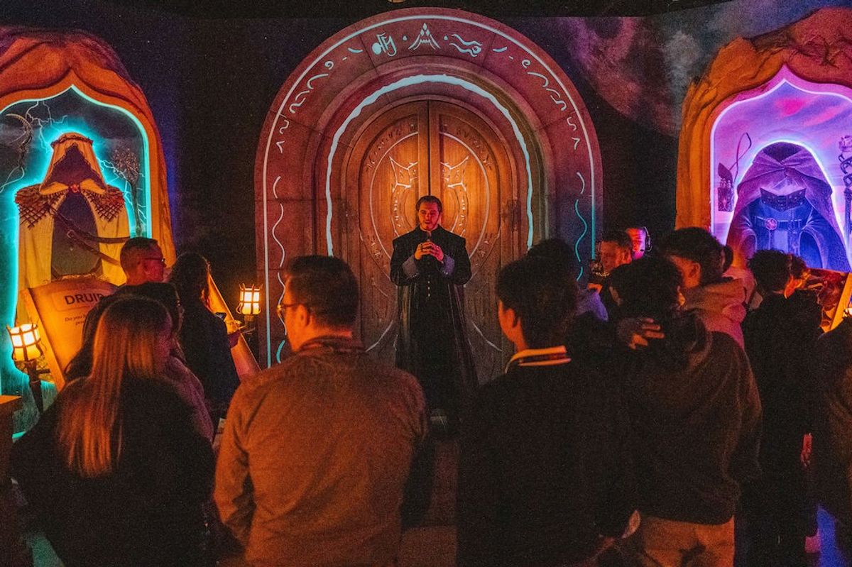 A group gathers around a costumed guide at a fantasy-themed exhibition with illuminated decor.