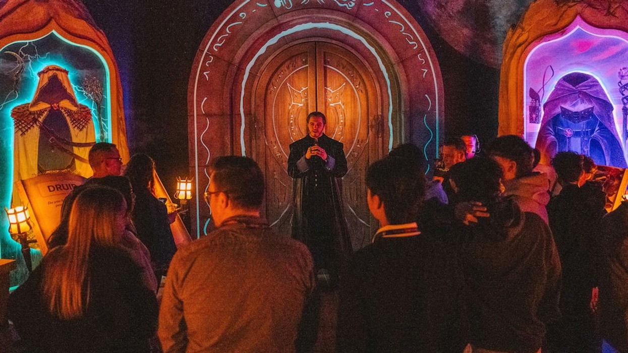 A group gathers around a costumed guide at a fantasy-themed exhibition with illuminated decor.