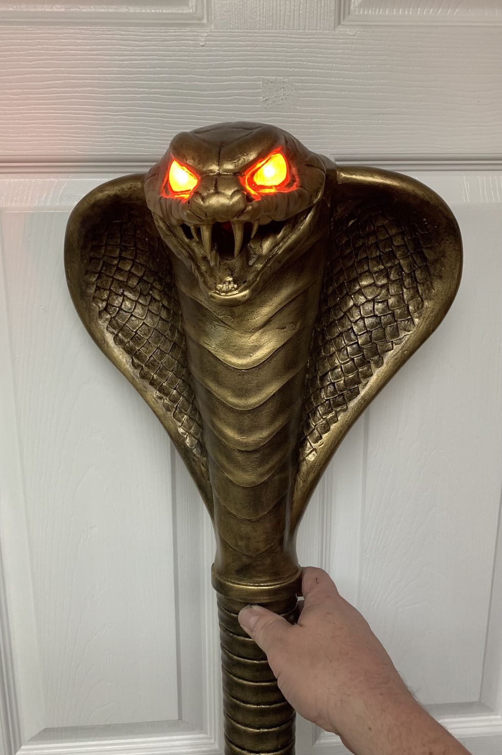 A hand holding a staff with a cobra head and glowing red eyes.