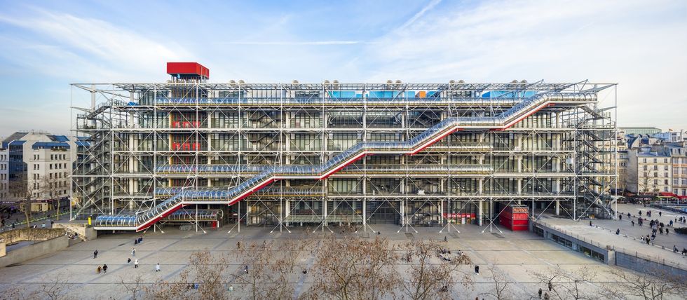 A large glass Centre Pompidou building wrapped in steel scaffolding, with a colorful diagonal escalator across its fa\u00e7ade.