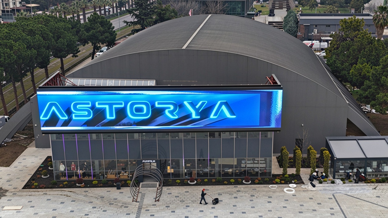 A large modern building with a curved roof and digital "ASTORYA" sign.