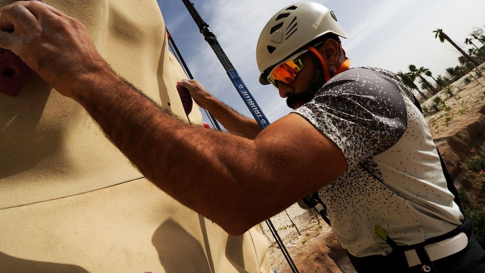 A man climbs a rock wall wearing a helmet and sunglasses at Adrena