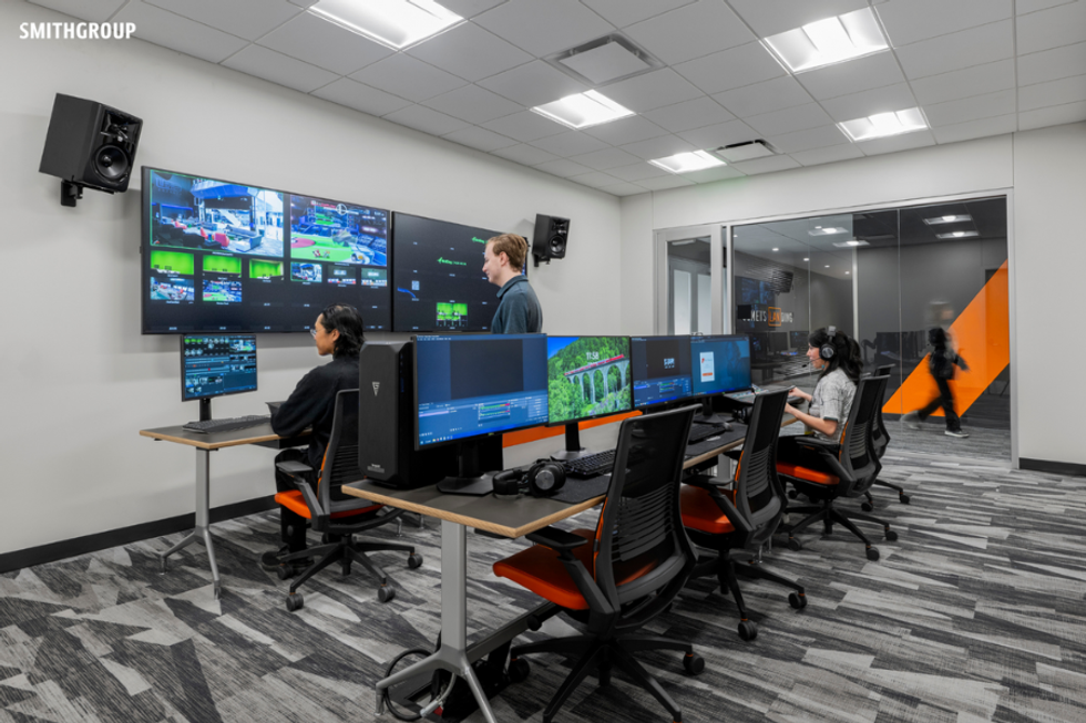 A modern esports room with people at desks and large screens displaying video games.