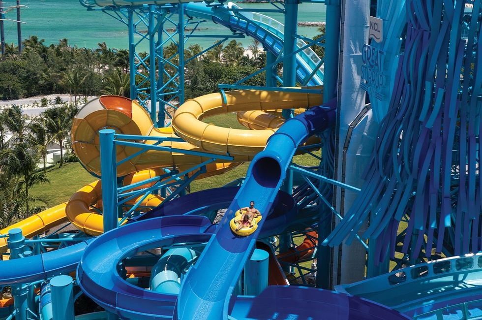A person enjoys a ride on a twisting blue water slide with lush greenery in the background at Great Tides Waterpark