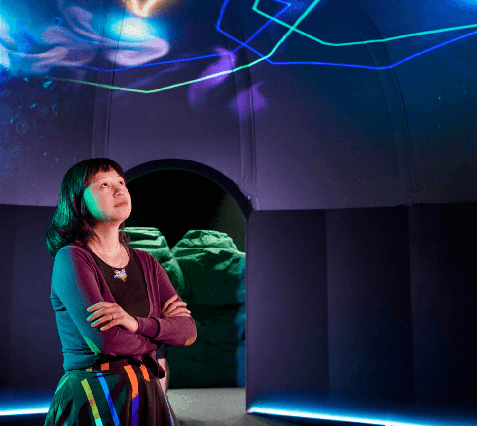 A person gazes upward in a dim room with colorful lights on the ceiling.