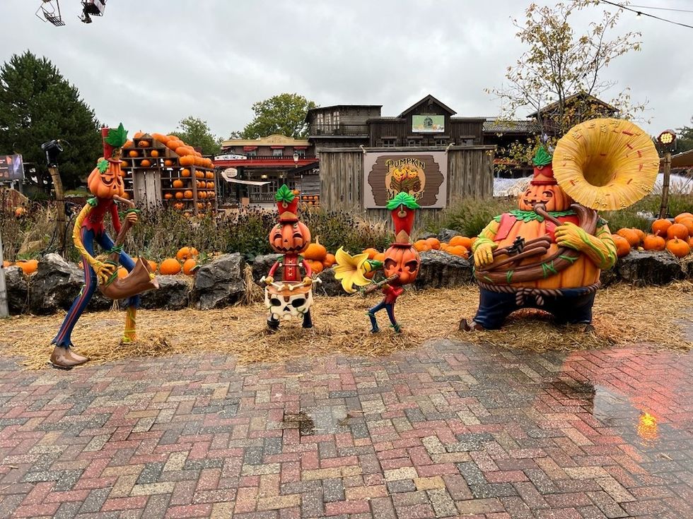 A pumpkin patch display features whimsical pumpkin characters, hay, and a rustic market building.