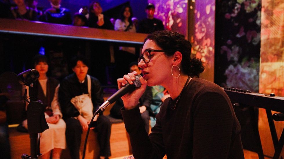 A singer performs on stage with a seated audience watching in a dimly lit venue.