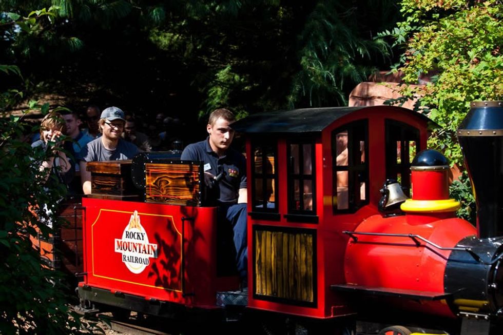 A small red train rides through a forest area with passengers aboard.