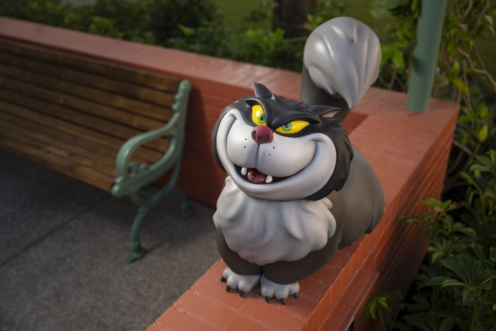 A statue of a grinning, cartoonish cat called Lucifer sits on a red brick wall near a bench at Disney World