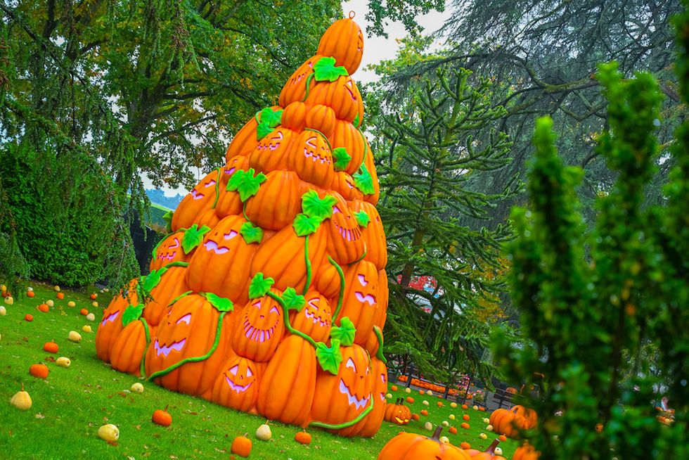 A towering pyramid of carved pumpkins decorated with green vines in a leafy park.