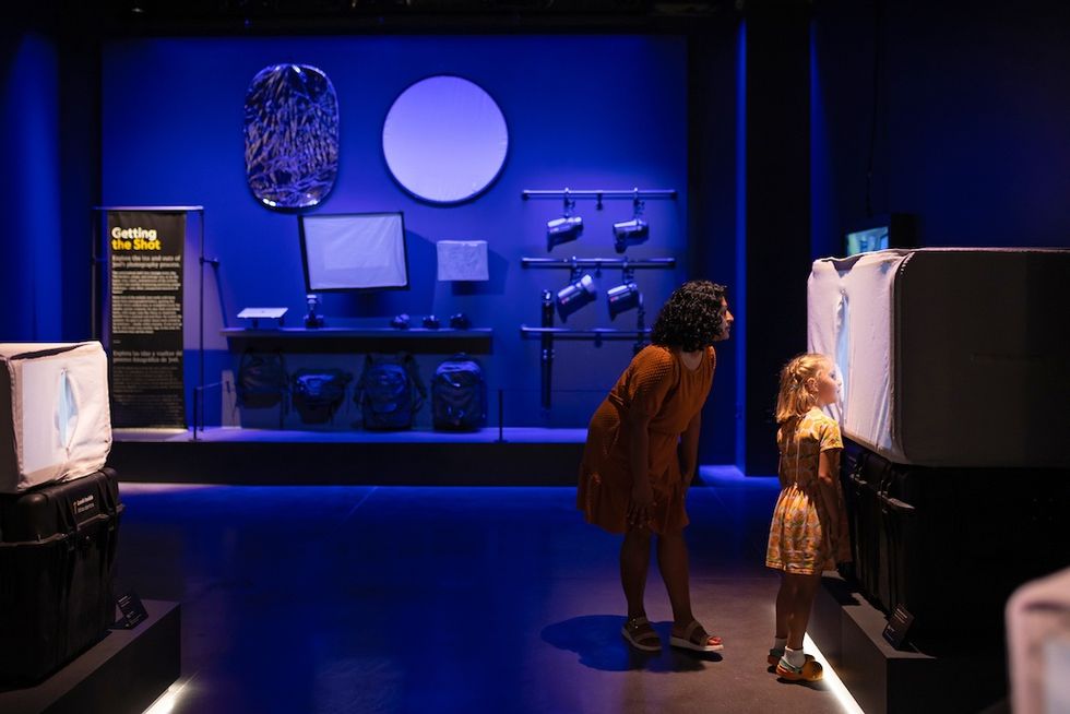 A woman and child explore a blue-lit interactive exhibit with photography equipment.