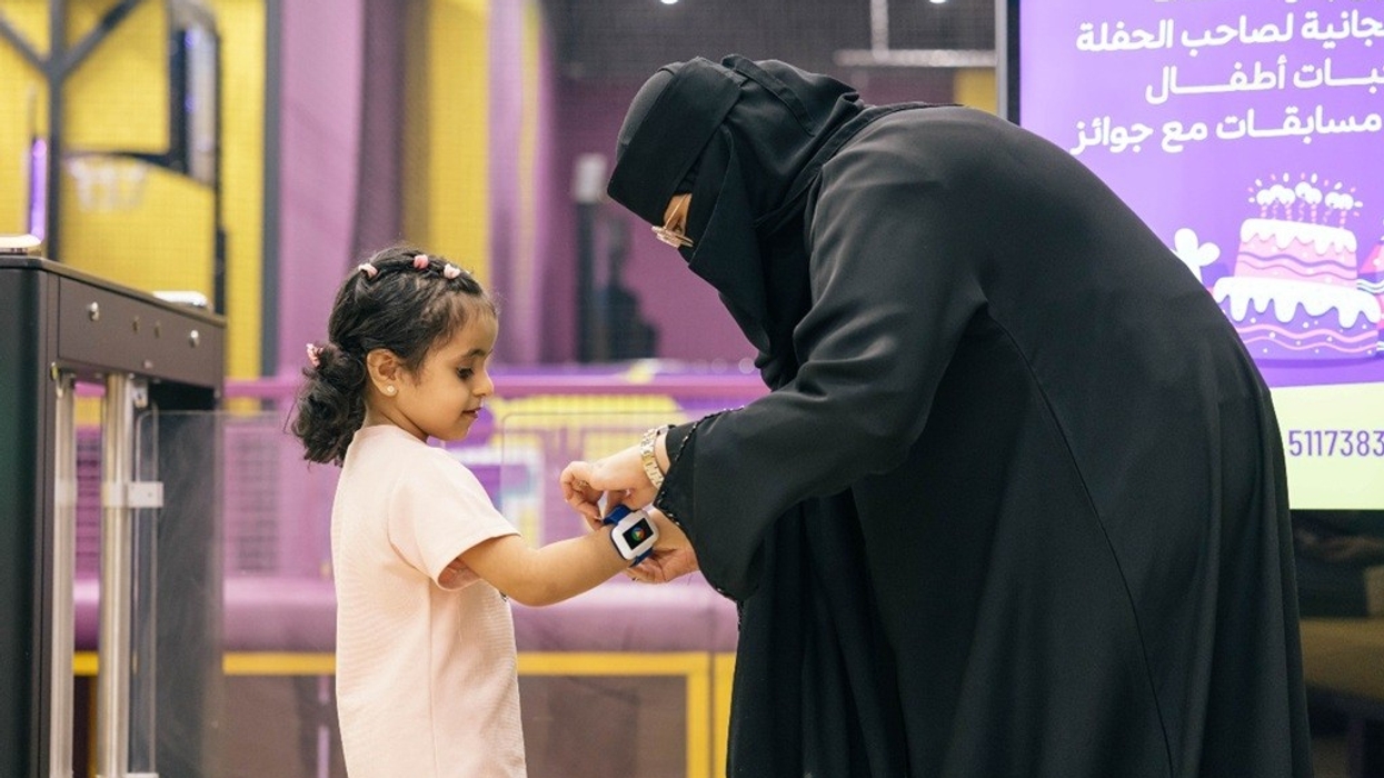 A woman helps a young girl with a wristband in a play area.