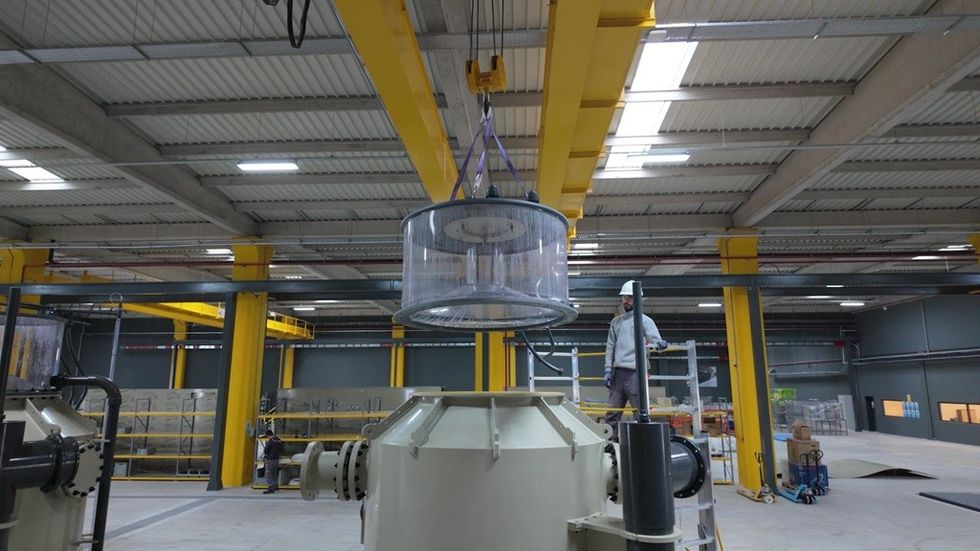 A worker operates a crane lifting equipment in a spacious industrial warehouse.