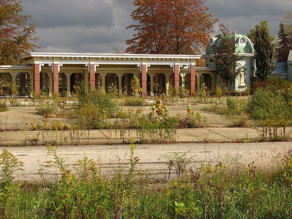 Abandoned building with overgrown vegetation and cloudy sky.