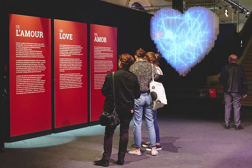 About Love exhibition visitors read panels about love, with a glowing blue heart displayed above.
