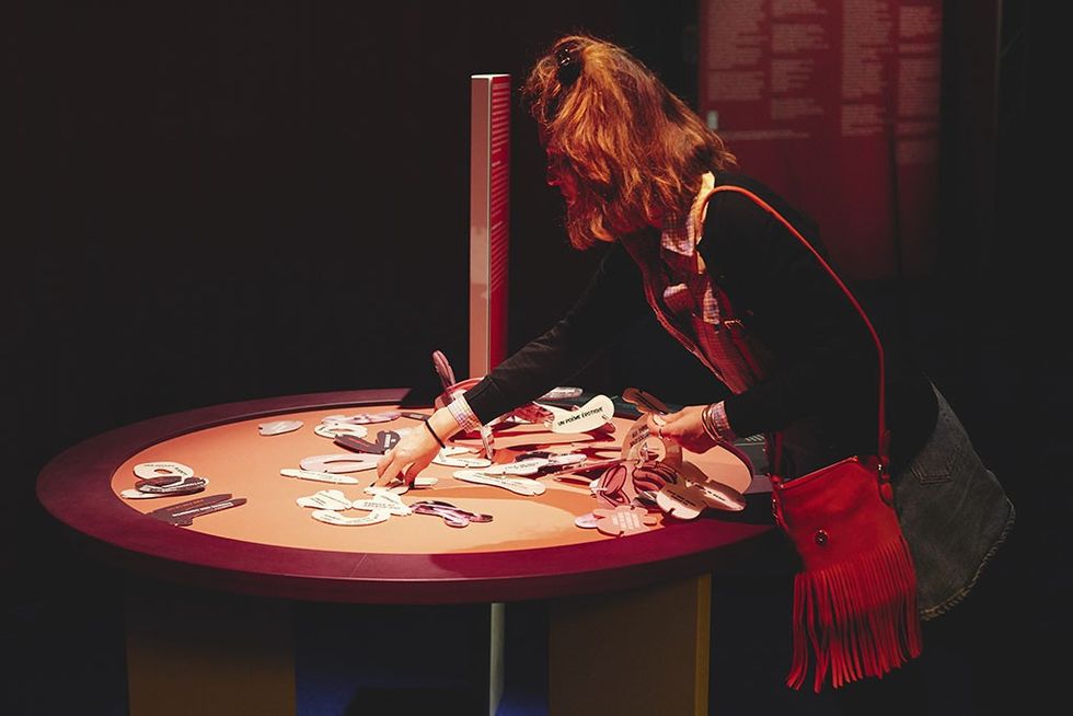 About Love exhibition - Woman interacts with pieces on a circular table, lit by a soft light.