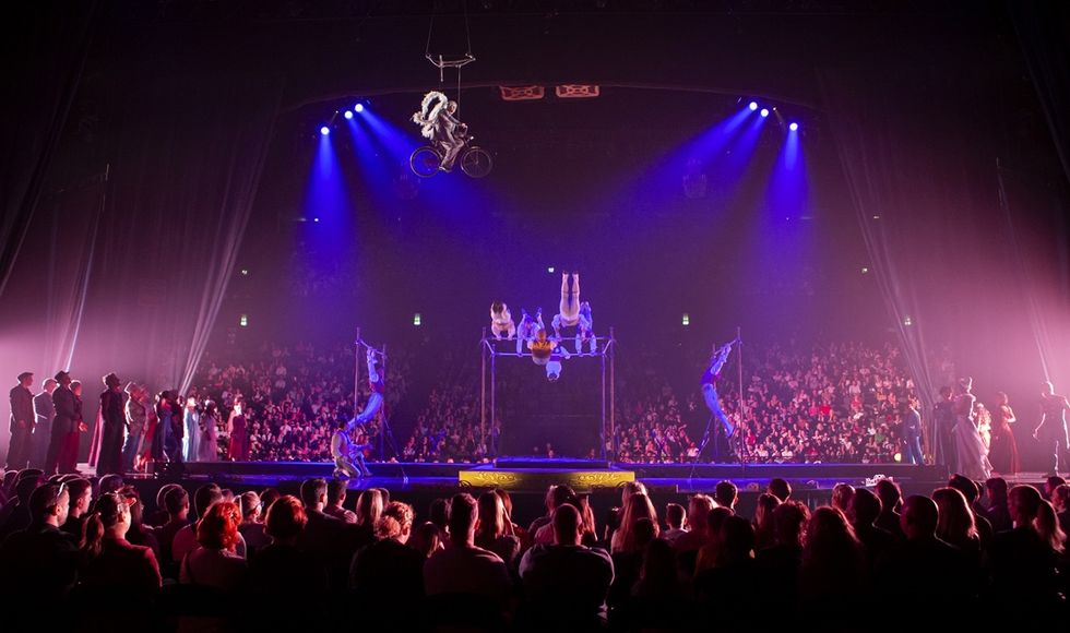 Acrobats performing on stage with audience watching, purple lighting in the background in Cirque du Soleil's Corteo.
