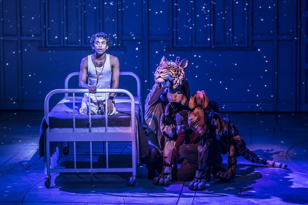 Actor with a tiger puppet on stage under starry lights.