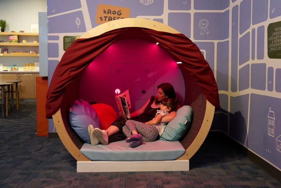 Adult and child reading together inside a cozy, circular pod with red lighting at Atlanta History Center