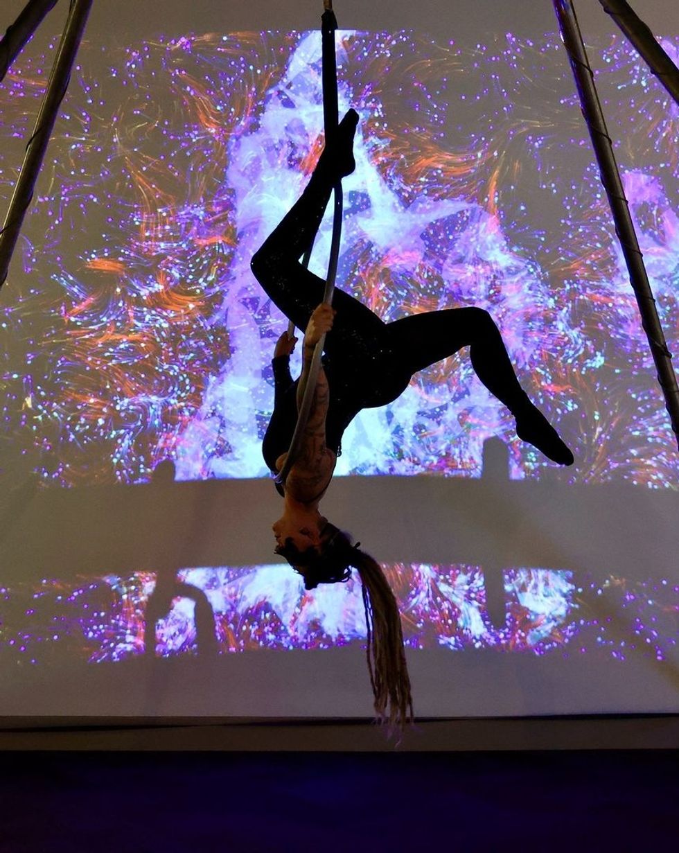 Aerial performer hangs upside down on silks with vibrant, colorful background projection from \u200bBreeze Creative