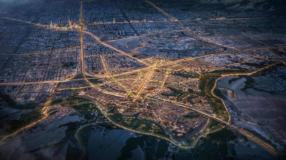 Aerial view of a city called Diriyah with illuminated roads at night, surrounded by dark landscape.