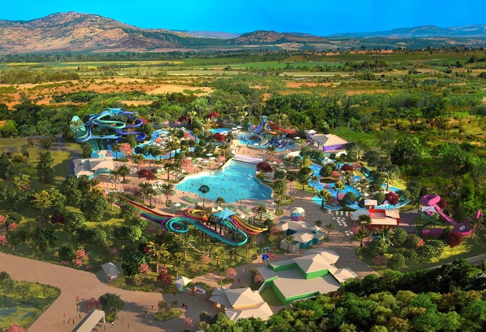 Aerial view of a colorful water park with slides and pools surrounded by lush green landscape.