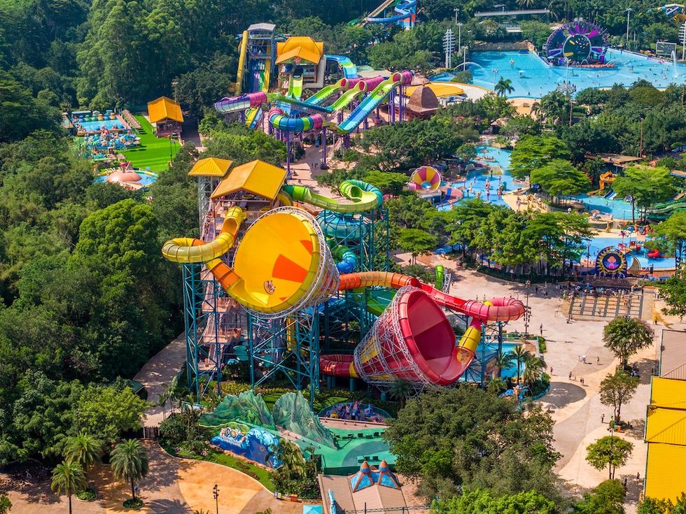 Aerial view of a colorful water park with slides and pools surrounded by lush greenery.