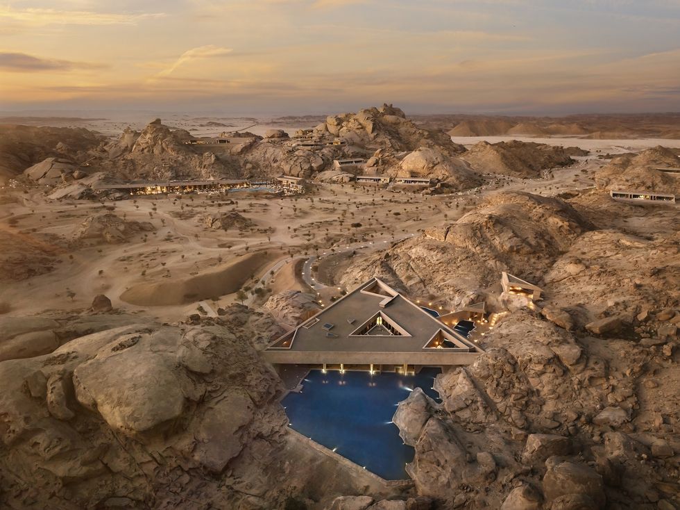 Aerial view of a desert resort with modern triangular architecture at sunset.