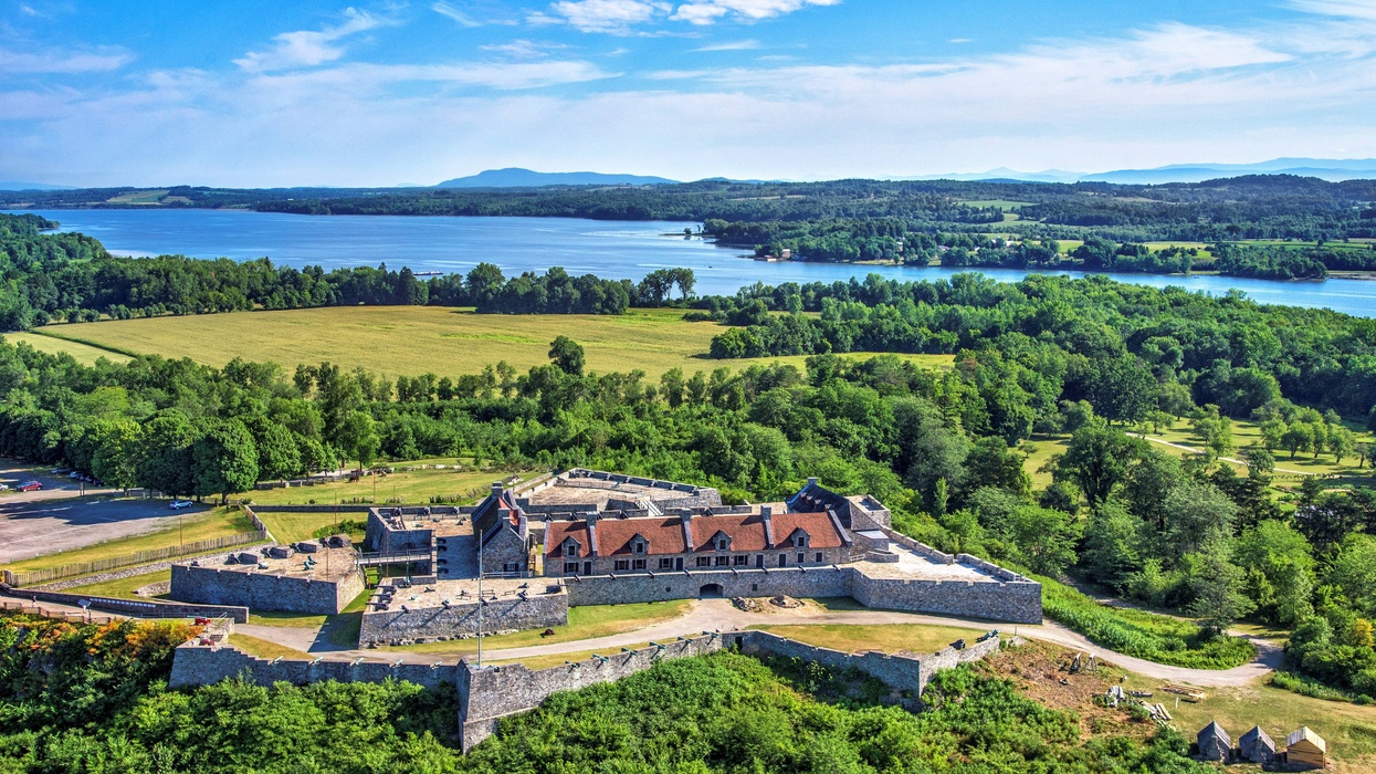 Aerial view of a historic fortress surrounded by lush greenery and a lake under a blue sky.