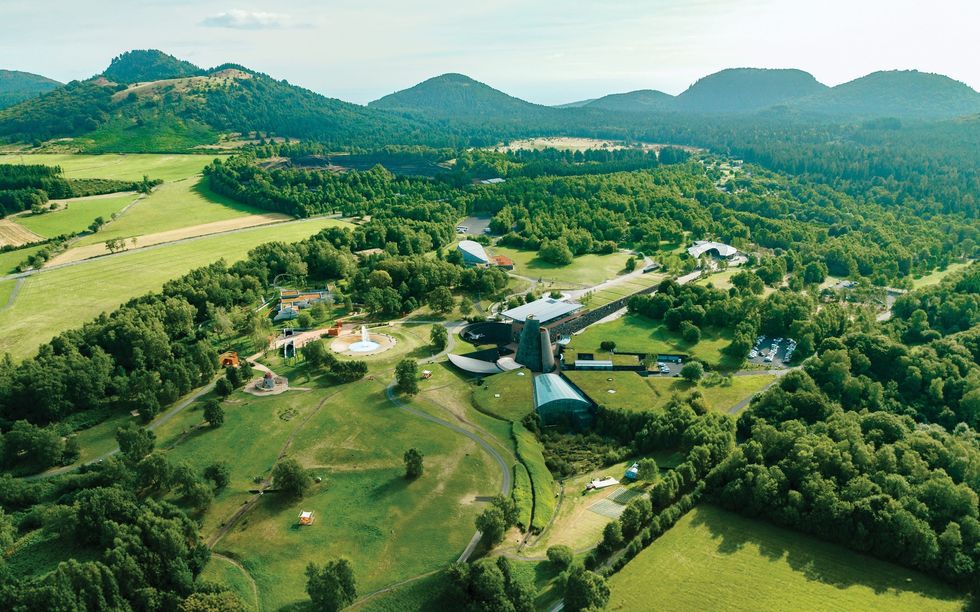 Aerial view of a lush, green valley with scattered buildings and distant hills at Vulcania
