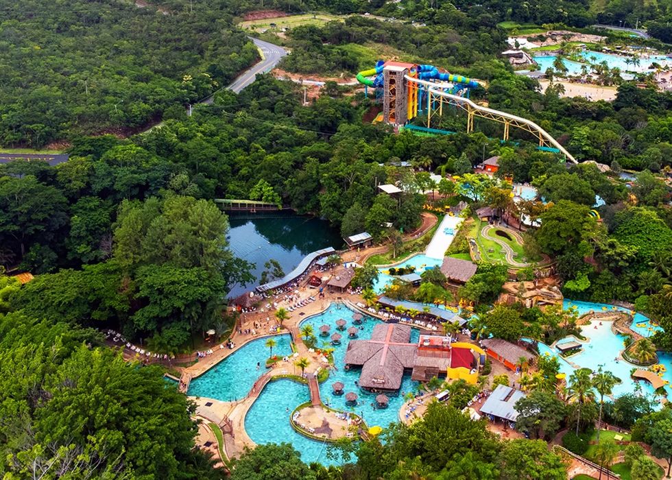 Aerial view of a lush water park called Hot Park with pools, slides, and surrounding greenery.
