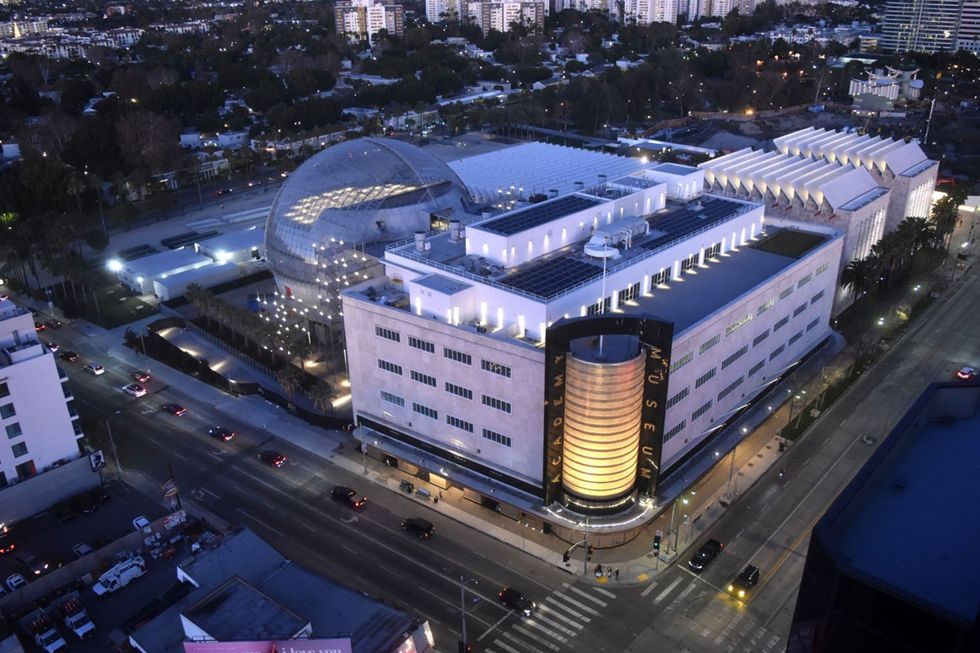 Aerial view of a modern building called the Academy Museum with a large illuminated dome at night.