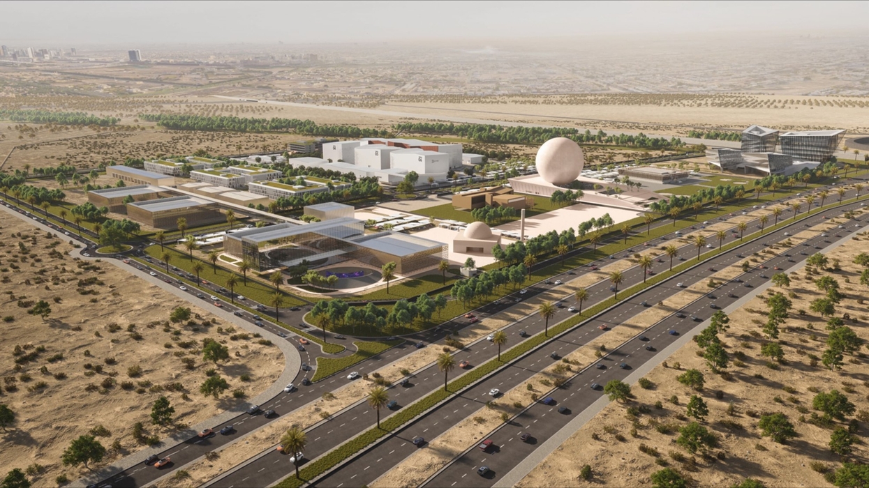 Aerial view of a modern building complex in a desert with surrounding roads and greenery.