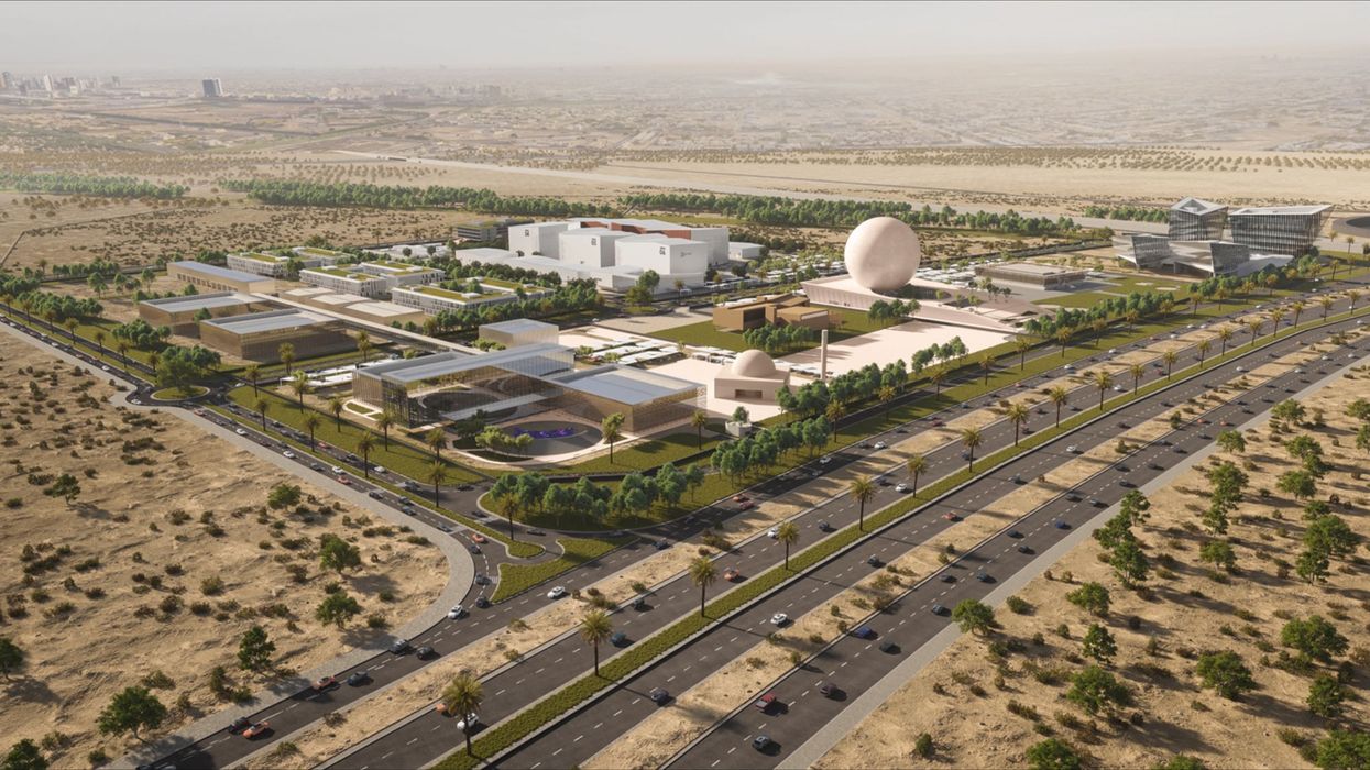 Aerial view of a modern building complex in a desert with surrounding roads and greenery.