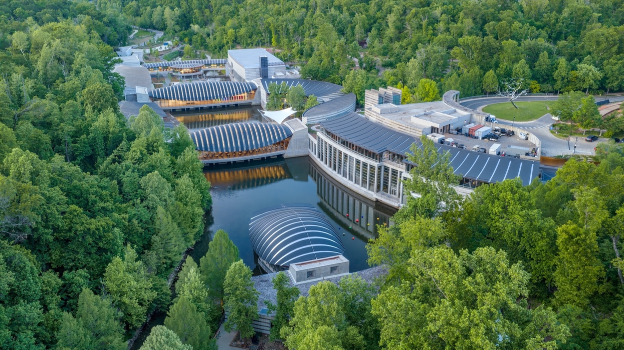 Aerial view of a modern, lakeside building complex called the Crystal Bridges Museum of American Art surrounded by lush greenery.
