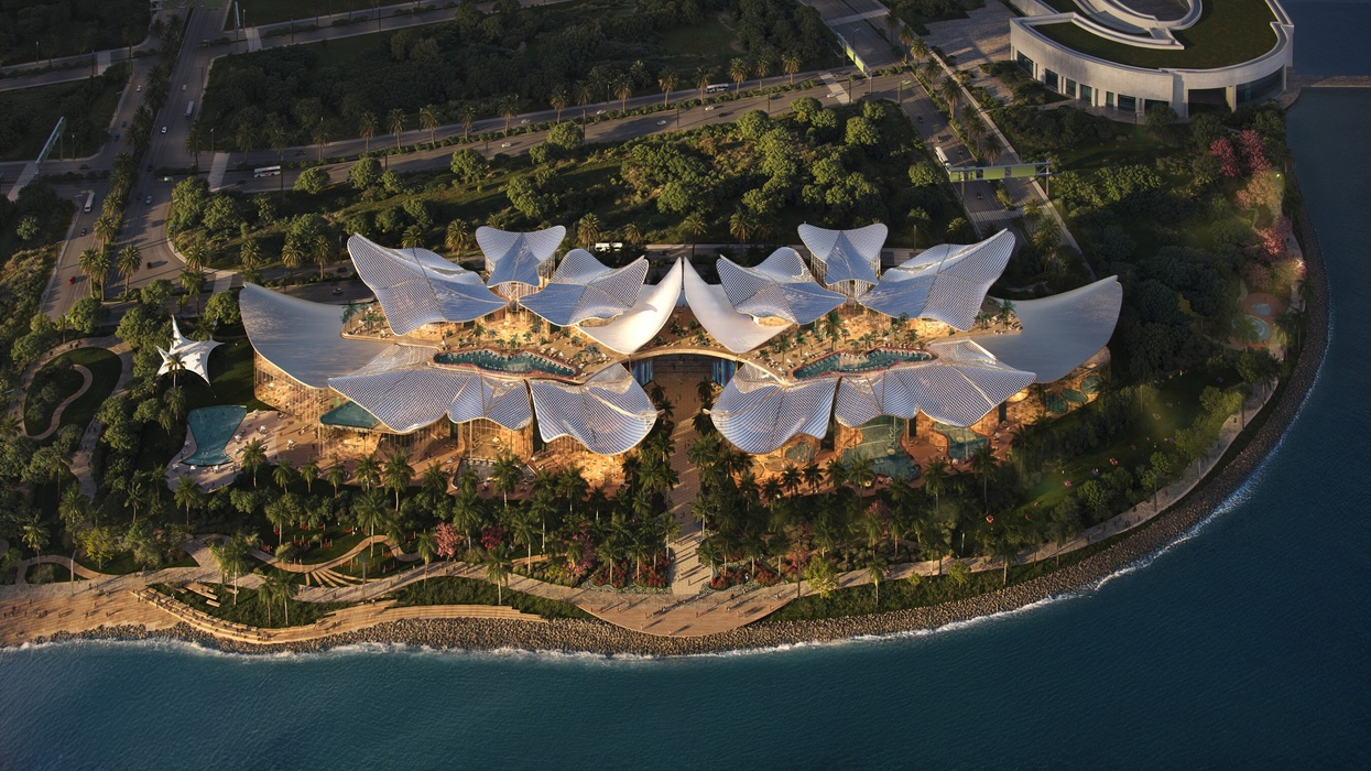 Aerial view of a modern, petal-shaped building called Therme Singapore by the waterfront, surrounded by trees.