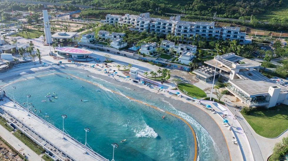 Aerial view of a PerfectSwell wave pool complex surrounded by modern buildings and greenery in Riyue Bay China