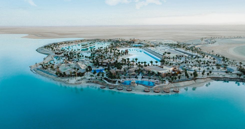 Aerial view of a resort island oasis called Adrena with pools, palm trees, and surrounding water