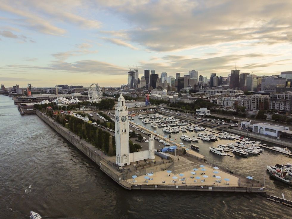 Aerial view of a riverside cityscape with a clock tower and marina at sunset.