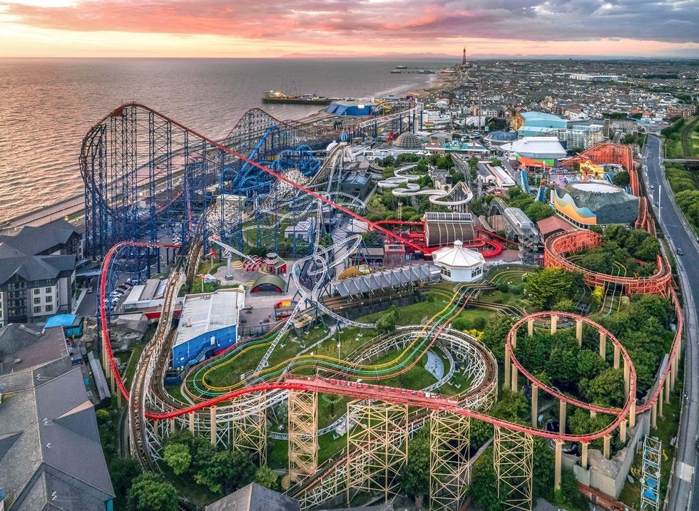 Aerial view of a seaside amusement park with roller coasters at sunset.