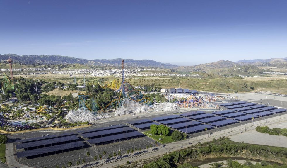 Aerial view of a solar panel field near a Six Flags amusement park and mountainous landscape.