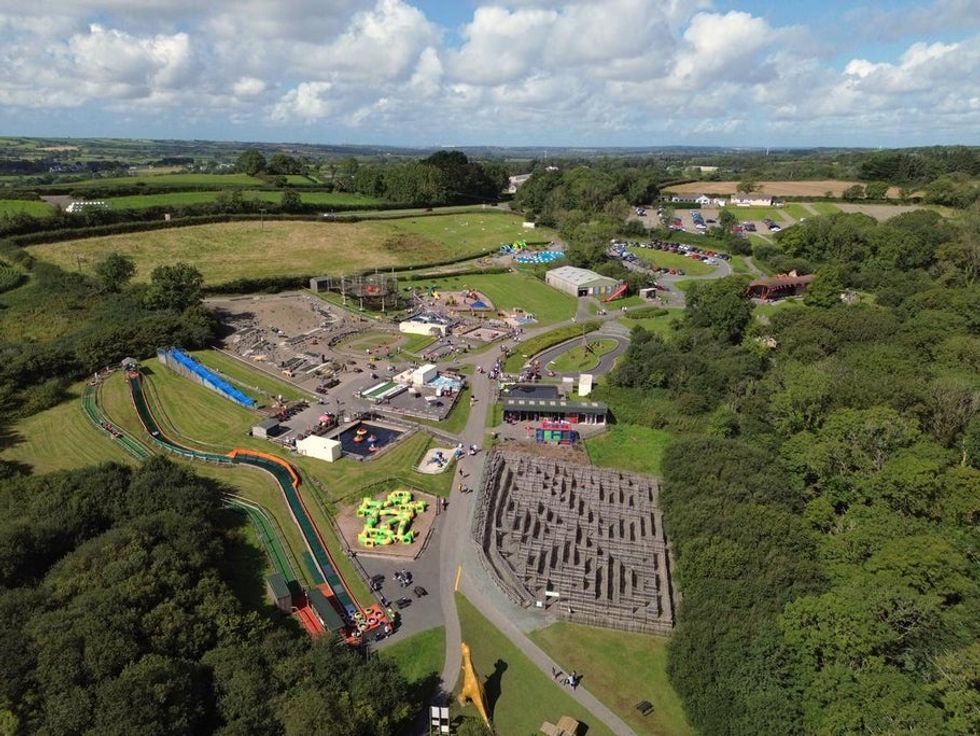 Aerial view of a theme park called the Dinosaur Park with a maze and slides, surrounded by green fields and trees.