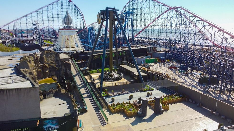 Aerial view of a theme park with roller coasters and a giant swing ride under a clear sky.