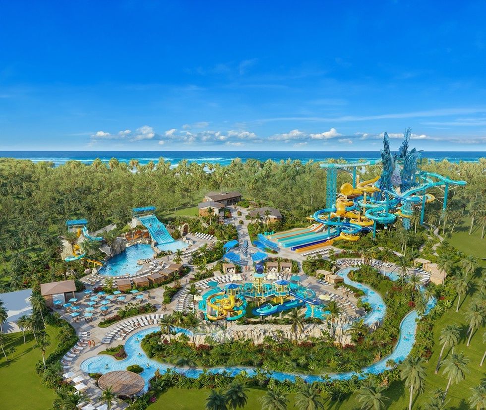 Aerial view of a tropical water park with slides, pools, and lush greenery near the ocean.