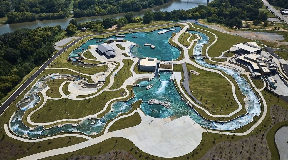 Aerial view of a twisting, clear water park with green lawns and a nearby river.